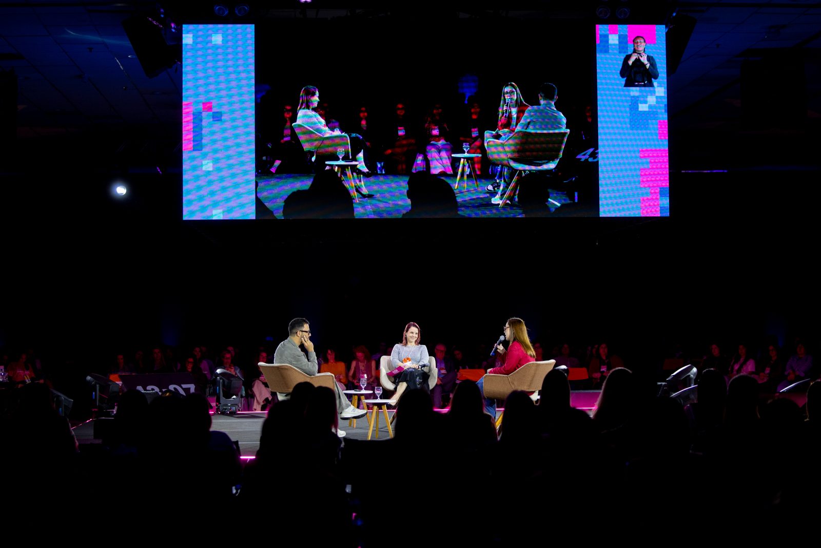 Marcus Rossi, Ali Silveira e Caroline Torma conversam no palco principal, com o telão ao fundo
