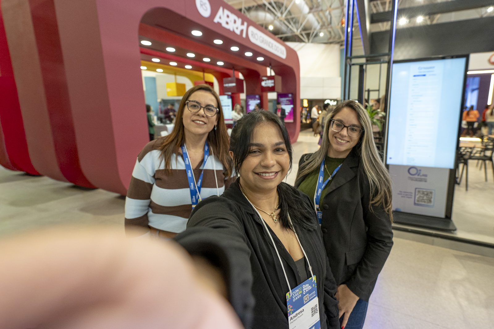 Três participantes fazem selfie em frente ao estande da ABRH-RS