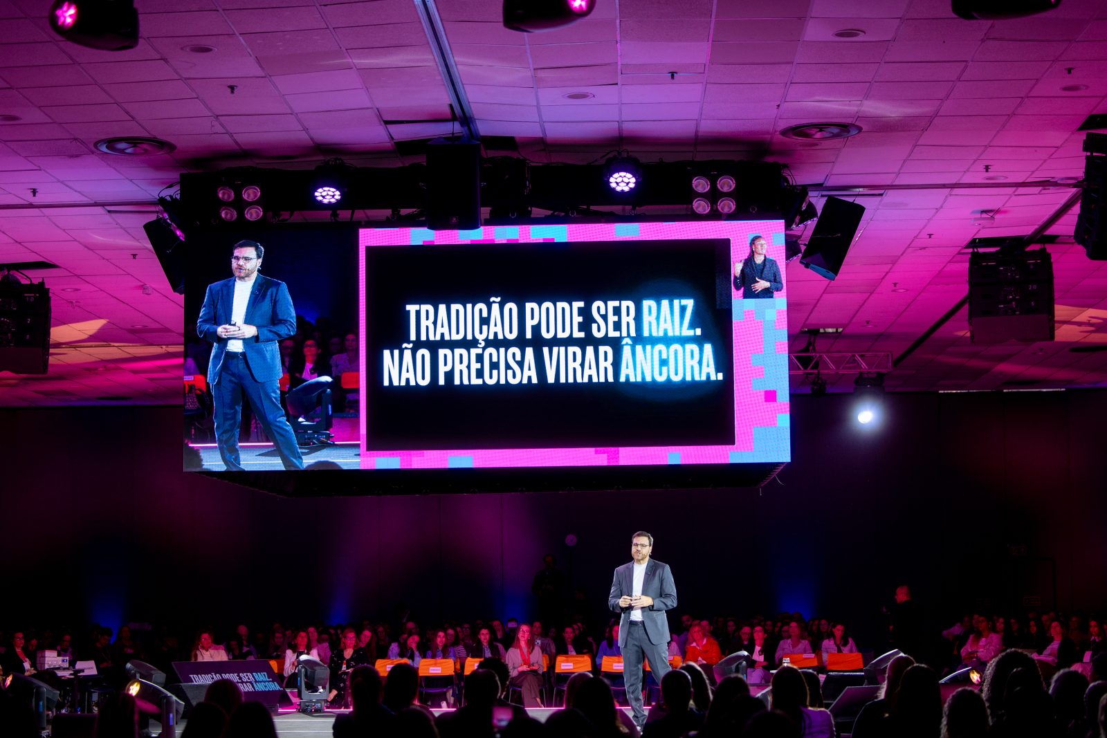 Henri Karam no palco principal, sob o telão com um slide da palestra