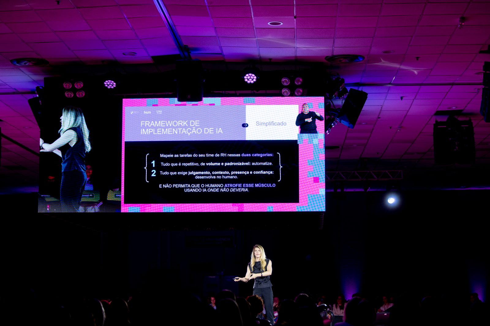 Letícia Setembro no palco principal, sob o telão com um slide sobre implementação de IA