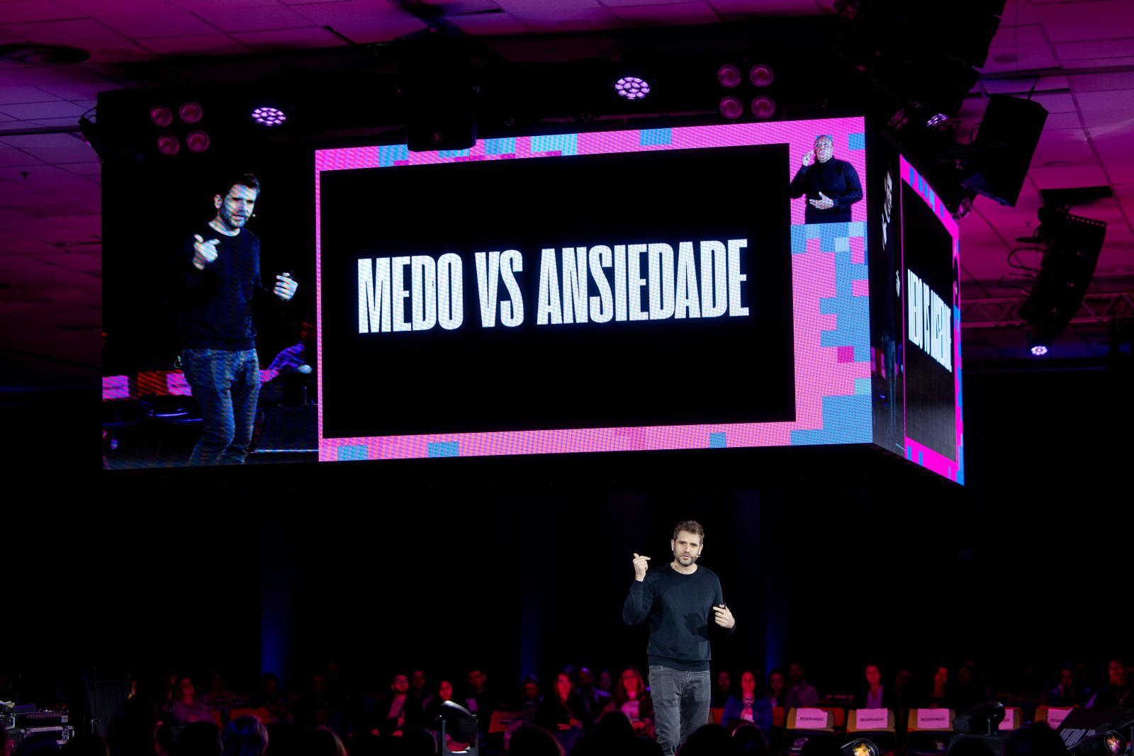 Emanuel Aragão no palco principal, sob o telão com o slide Medo vs ansiedade